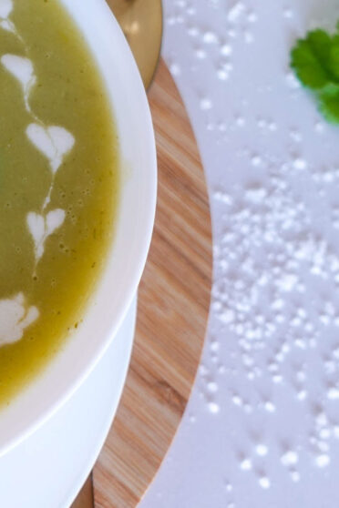 A bowl of potato leek soup on a wooden board and greens on another board.