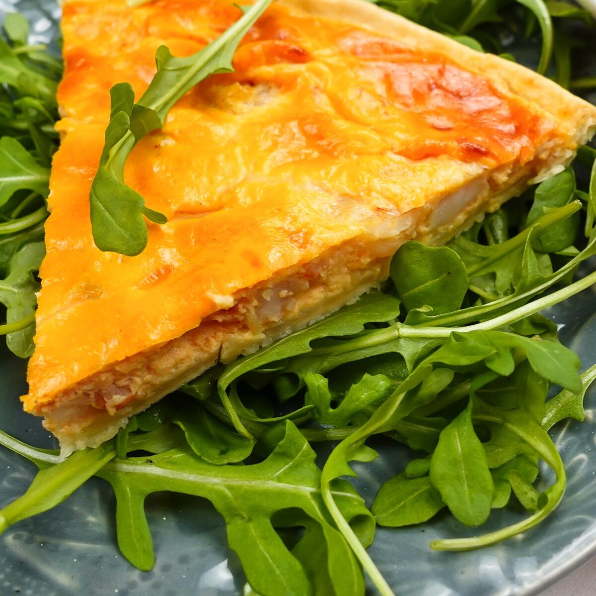 A piece of shrimp quiche on a plate with arugula.