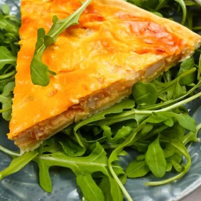 A piece of shrimp quiche on a plate with arugula.