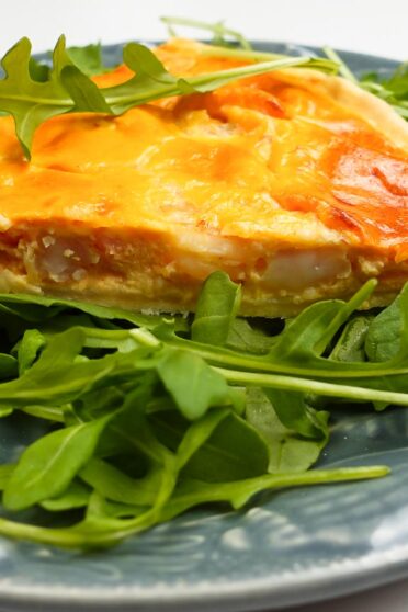 Ready shrimp quiche on a plate with fresh arugula.