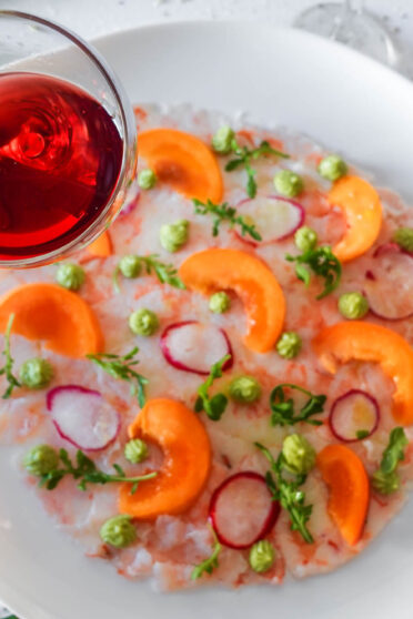 Apricot Shrimp Carpaccio on a plate with a glass of wine in a left hand