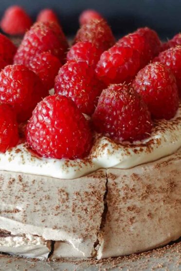 Raspberry Pavlova on a plate with fresh raspberries on a side.