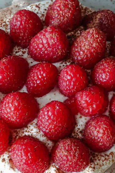 Raspberry Pavlova on a plate with fresh raspberries on a side.