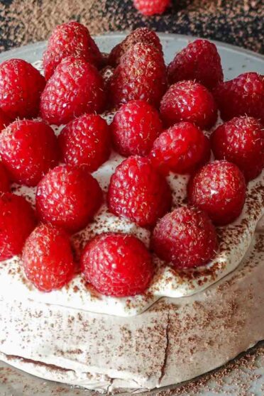 Raspberry Pavlova on a plate with fresh raspberries on a side.