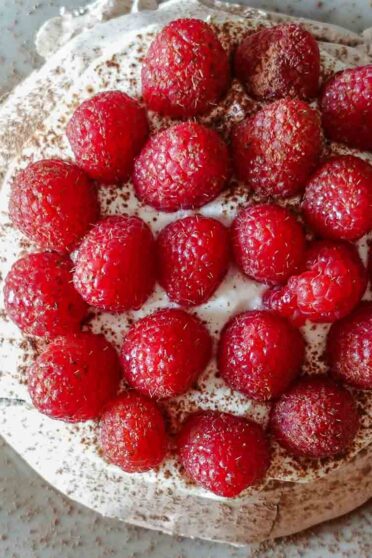 Raspberry Pavlova on a plate with fresh raspberries on a side.