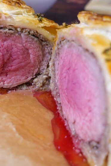 Cut Beef Wellington on a board with juicy meat inside.