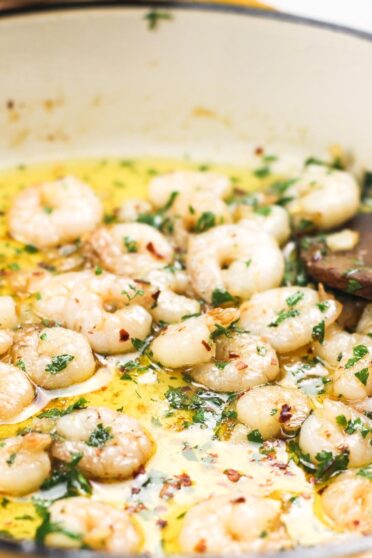 Shrimp in garlic sauce in a pan with a wooden spoon inside.