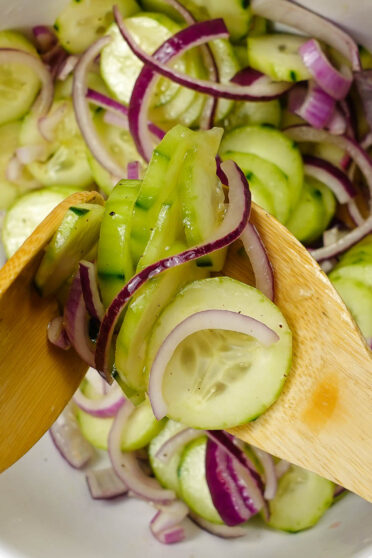 Cucumber Red Onion Salad Recipe in a big white bowl with a wooden fork and spoon.