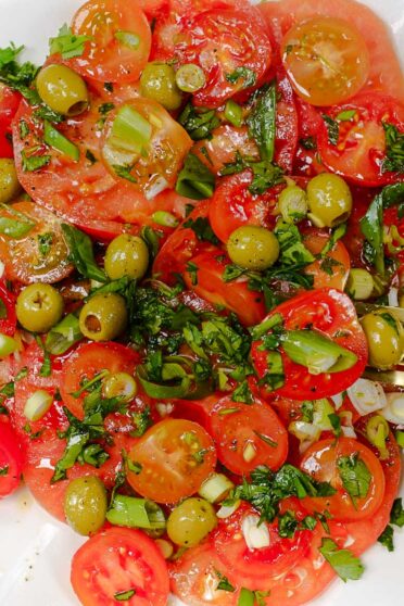Mediterranean Tomato Salad on a plate and a fork full of salad in right hand.
