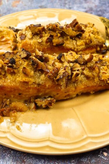 A closeup of delicious Pecan Crusted Salmon on a yellow plate with fork and knife.