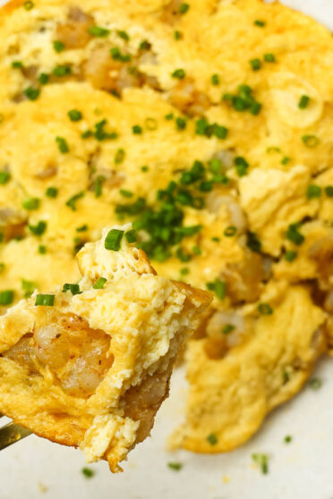 Shrimp Omelette on a plate with green onion and a fork full of omelette.