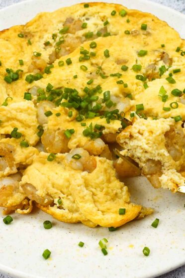 Shrimp Omelette on a plate with green onion and a fork full of omelette.
