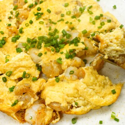 Shrimp Omelette on a plate with green onion and a fork full of omelette.