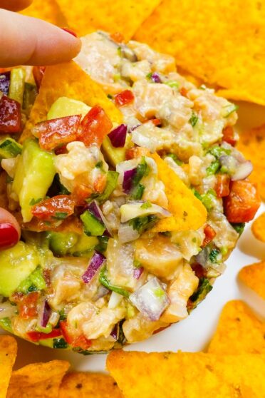 Spicy Salmon Tartare with Corn Chips on a white plate and one chip with spicy salmon tartare in one hand.