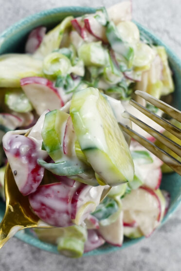 Creamy Cucumber Radish Salad in a bowl with a spoon and fork.