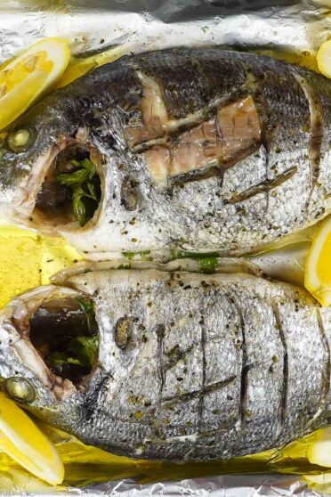Foil baked Sea Bream with fresh lemon slices on a tray, in two hands.