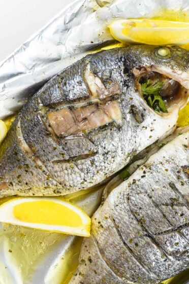 Delicious Foil baked Sea Bream with fresh lemon slices on a tray.