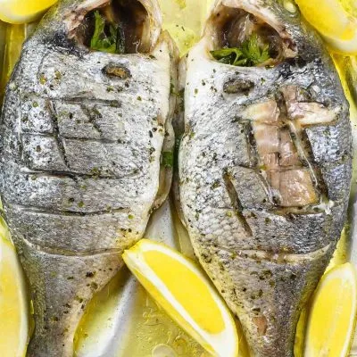 Foil baked Sea Bream with fresh lemon slices on a tray.