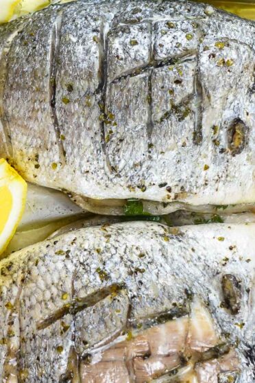 Foil baked Sea Bream with fresh lemon slices on a tray.