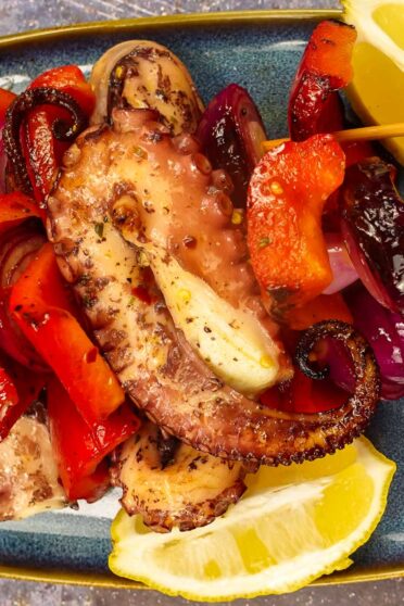 Mouthwatering Grilled Octopus Skewers on a plate with fresh lemon slices.