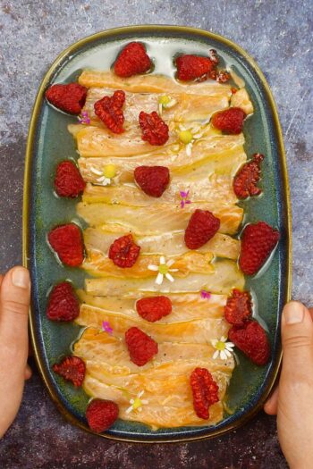 Flavorful Salmon Crudo with Raspberries on a plate in two hands.