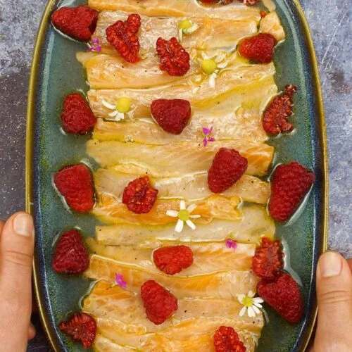 Flavorful Salmon Crudo with Raspberries on a plate in two hands.