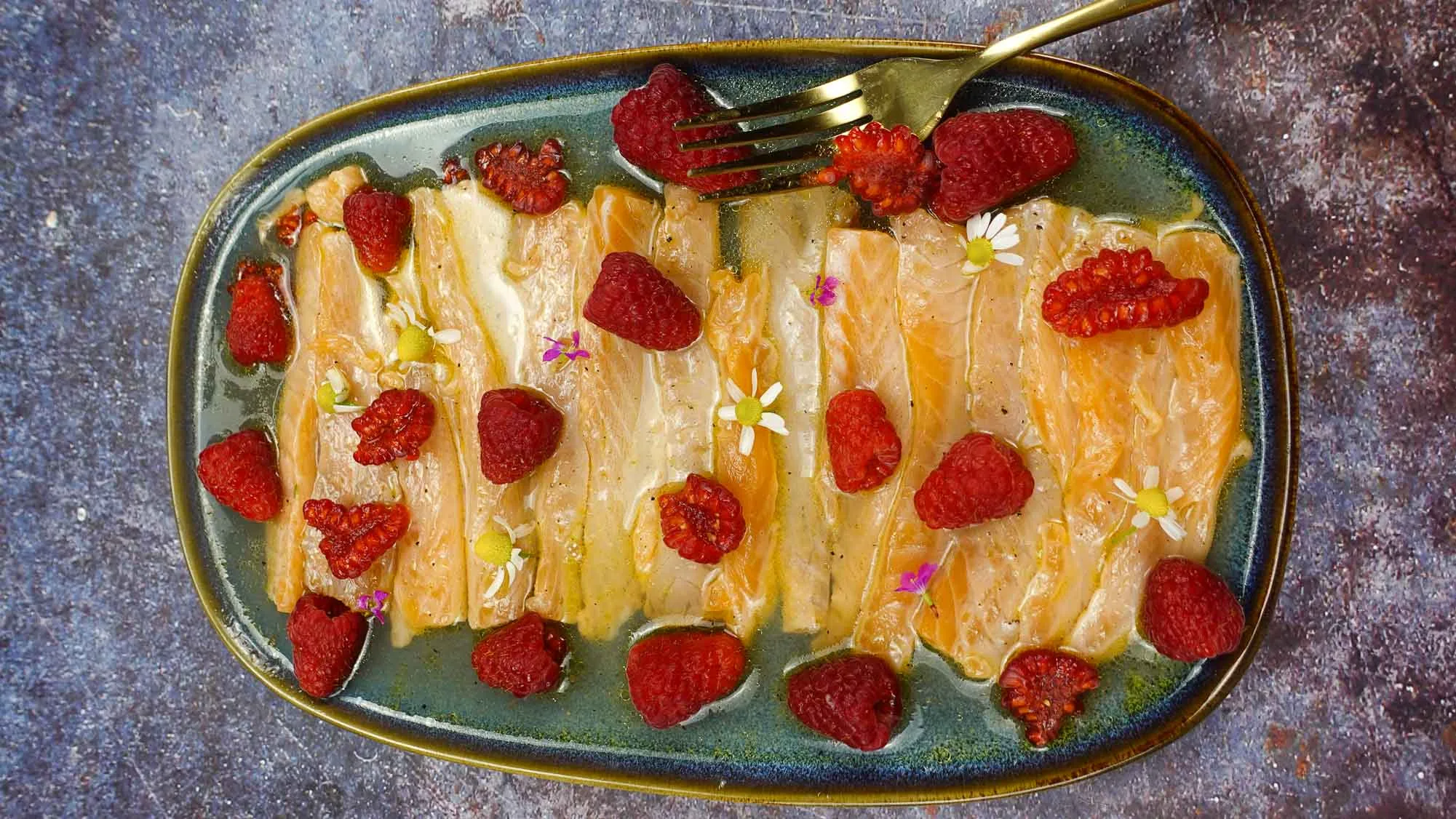 Flavorful salmon crudo with raspberries on a plate with a fork.
