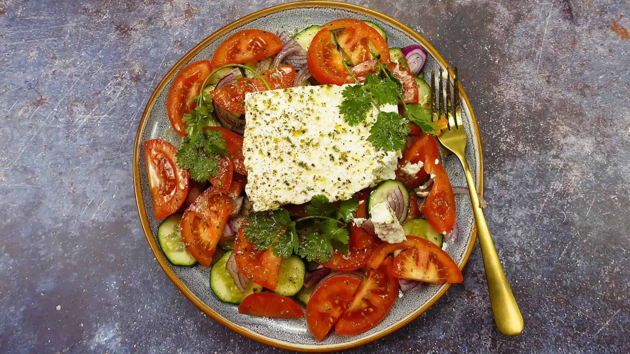 Flavorful tomato cucumber feta salad on a plate with a fork from the right side.