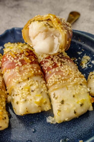 A closeup of Mediterranean Baked Fish Fillets on a blue plate with a piece of flaky fish