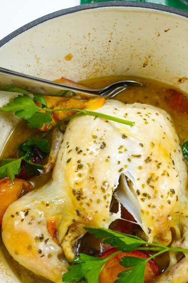 A close up of chicken with lots of juices in green dutch oven