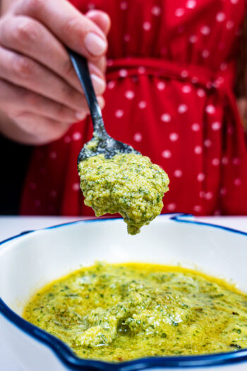 Fresh basil Pesto in a bowl and one spoon on top of the bowl
