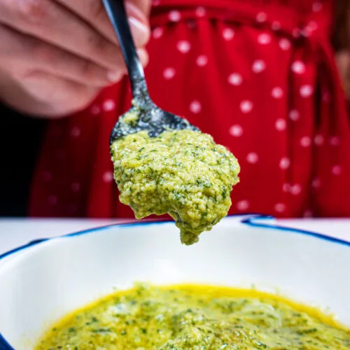 Fresh basil Pesto in a bowl and one spoon on top of the bowl