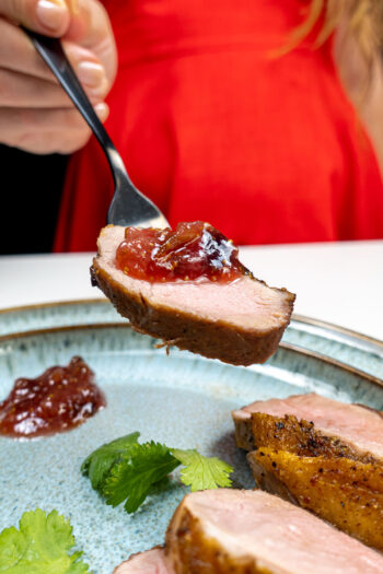 Pan Fried Duck Recipe with fig jam on top of one piece on a plate with fresh cilantro