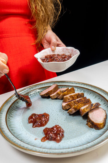 Perfectly cooked duck on a plate with fig jam. Helena is adding sauce on the plate.