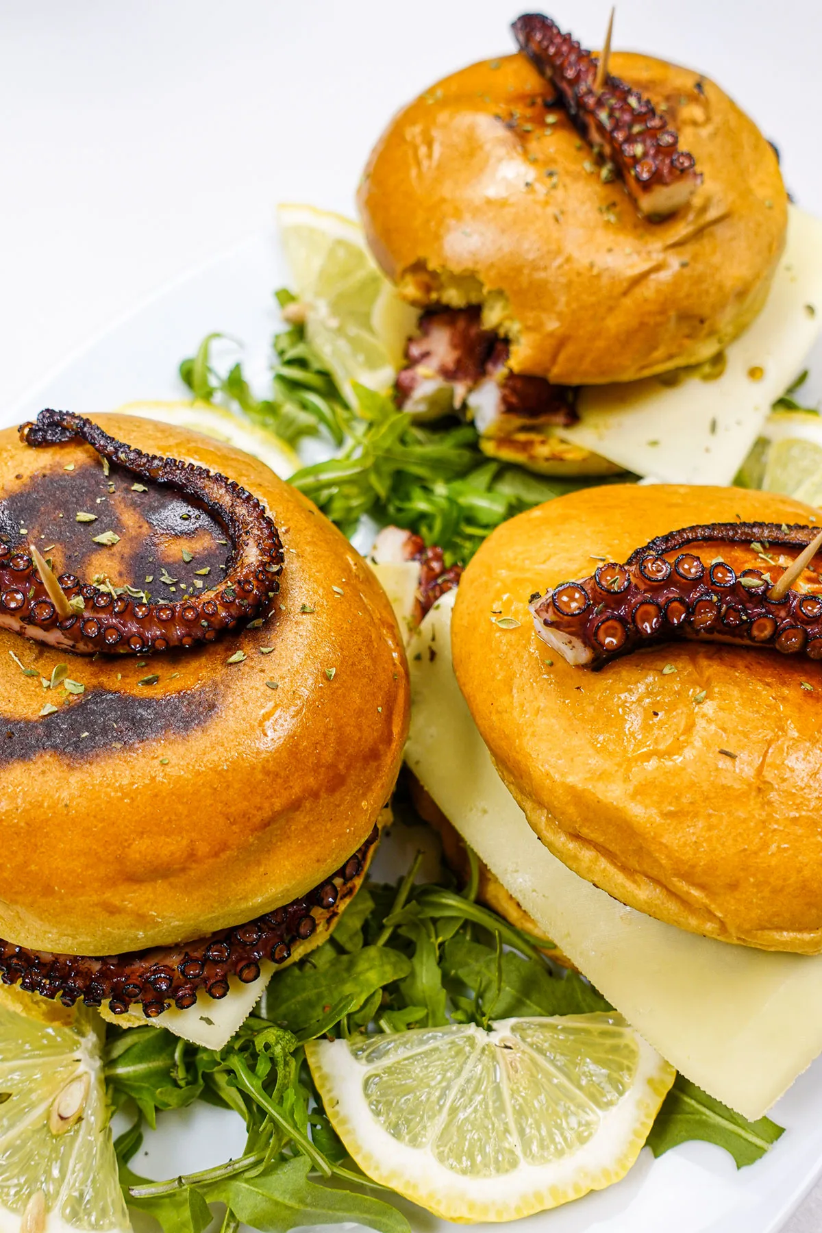 Three octopus burgers on a plate with arugula and lemon slices