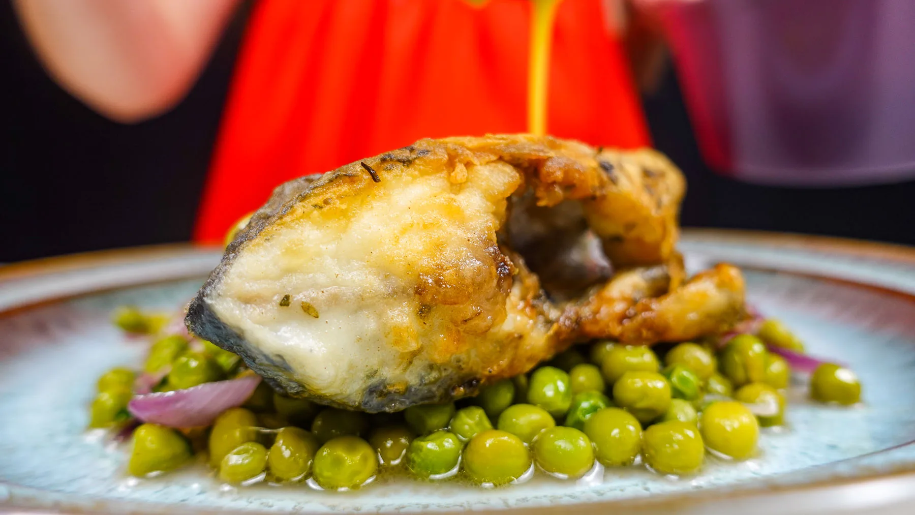 Helena is serving pan fried sea bream with sauce and green peas on a plate