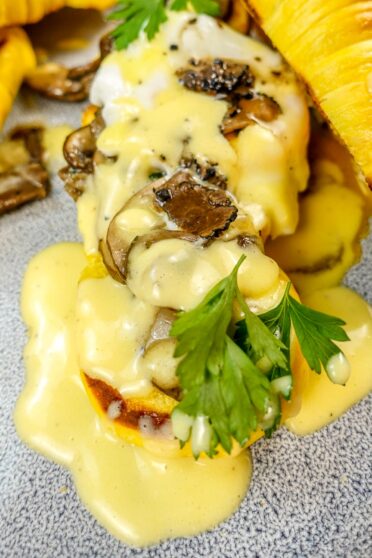 A closeup of one croissant with hollandaise sauce and black truffle and parsley on top