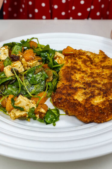 Helena is holding a plate in two hands with juicy cutlet and colorful fall salad