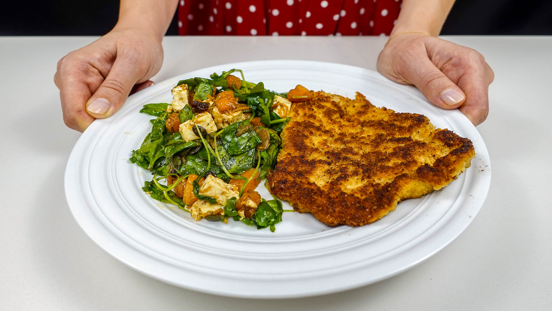Helena is holding a plate in two hands with juicy cutlet and colorful fall salad