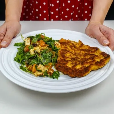 Helena is holding a plate with juicy turkey cutlet with pumpkin salad on white plate