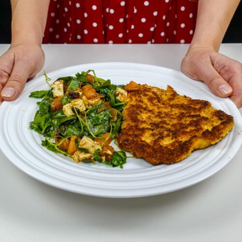 Helena is holding a plate with juicy turkey cutlet with pumpkin salad on white plate
