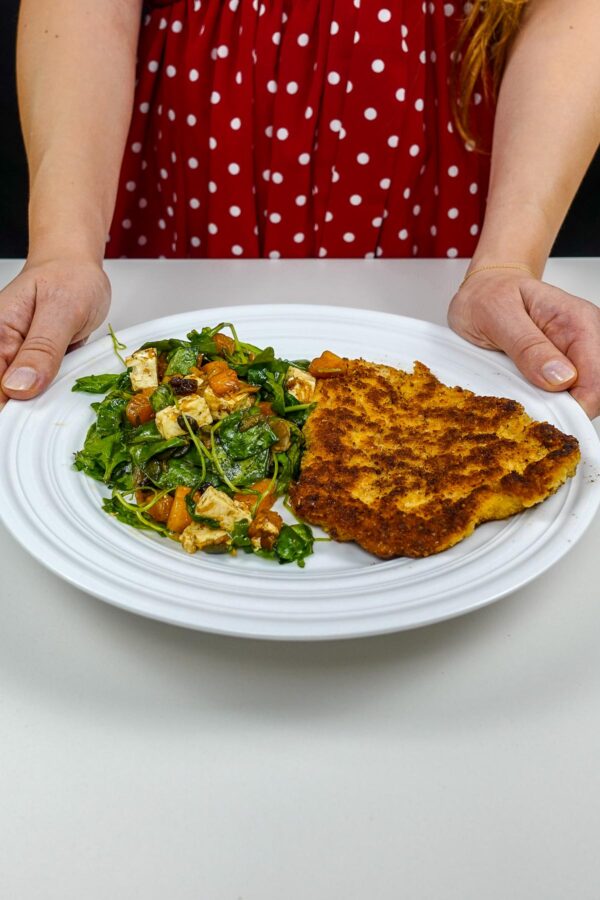 Helena is holding a plate with juicy turkey cutlet with pumpkin salad on white plate