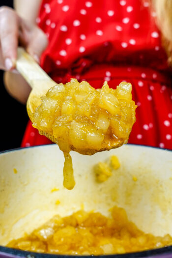 Helena is holding a spoon with a ready golden pear jam over the pot