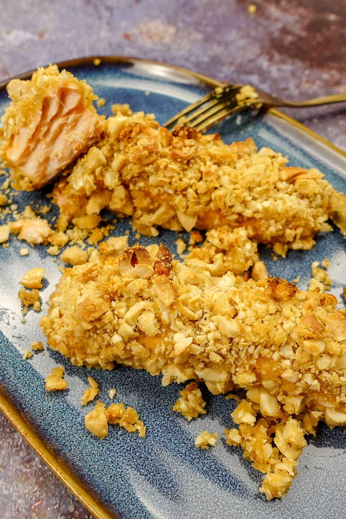 Two pieces of cashew crusted salmon on a blue plate with a fork