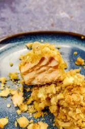 Two pieces of cashew crusted salmon on a blue plate with baked cashew around