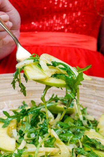 Helena is holding a fork full of fennel apple salad over the bamboo bowl full of salad