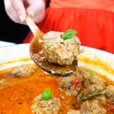 Helena is holding a wooden spoon with meatball over the skillet with meatballs