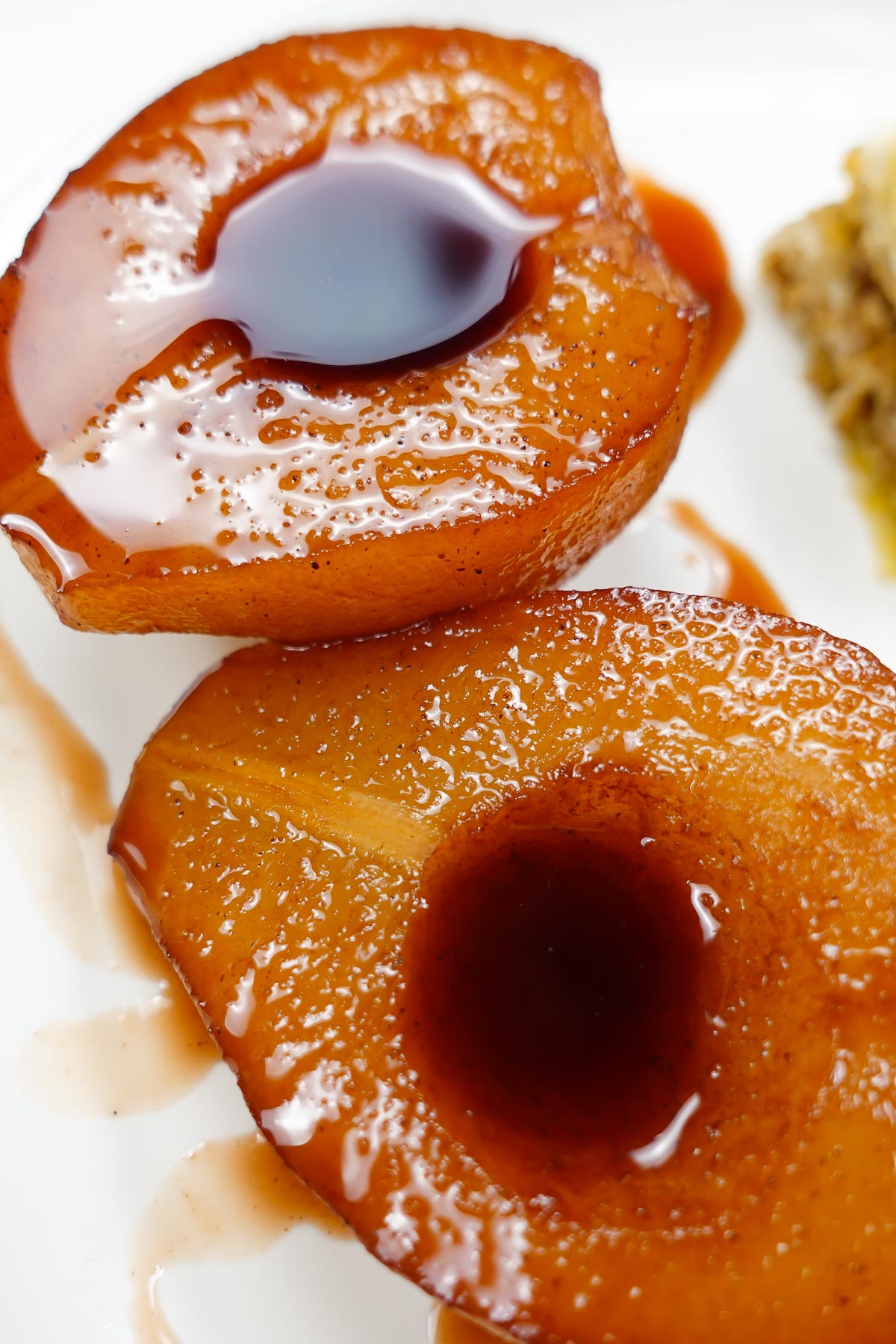 A closeup of two pears on a white plate with syrup.