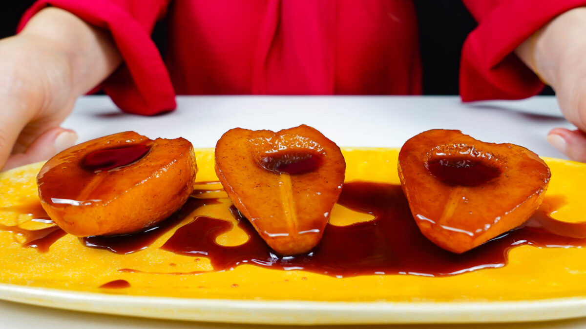 Port Wine Poached Pears with syrup on a yellow plate in two Helena's hands.