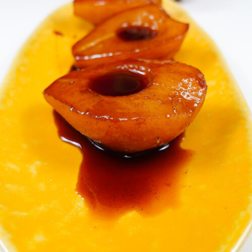Port Wine Poached Pears with syrup on a yellow plate.